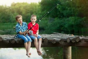 le garçons asseoir sur une en bois pont et poisson. les enfants sur une pêche voyage. photo