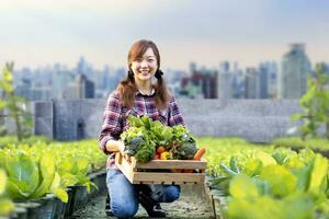 une agricultrice asiatique porte le plateau en bois rempli de légumes biologiques fraîchement cueillis dans son jardin pour la saison des récoltes et un concept d'alimentation saine photo