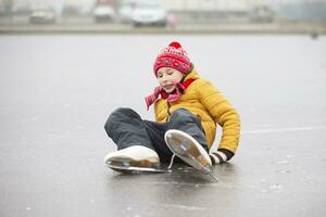 une peu garçon est tombée lorsque il a été apprentissage à skate.a enfant sur un la glace patinoire. photo