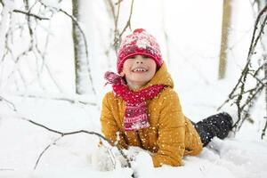 marrant peu garçon dans coloré vêtements en jouant en plein air pendant une chute de neige. actif vacances avec les enfants dans hiver sur du froid neigeux jours. content enfant est ayant amusement et en jouant dans l'hiver. photo