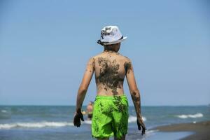 une garçon enduit dans guérison noir magnétique le sable entre dans le mer. photo