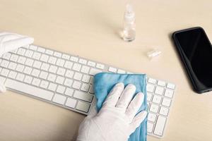 main avec gant de protection nettoyant un clavier avec un désinfectant photo