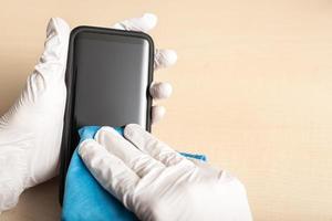 mains avec des gants nettoyant le téléphone portable avec un désinfectant photo