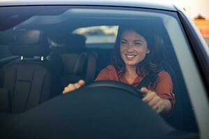 magnifique Jeune femme conduite sa Nouveau voiture à le coucher du soleil. femme dans auto. proche en haut portrait de agréable à la recherche femelle avec heureux positif expression, femme dans décontractée porter conduite une voiture photo