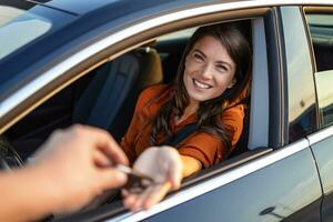 optimiste femelle client séance dans marque Nouveau voiture et prise clés de surgir Marchand dans concession. femme faire achat dans voitures salle d'exposition. elle est assis à l'intérieur de magnifique voiture et Regardez à Ventes agent photo