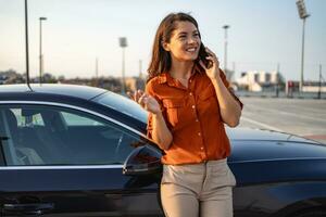 femme en utilisant mobile téléphone, la communication ou en ligne application, permanent près voiture sur ville rue ou parking, en plein air. voiture partage, de location un service ou Taxi application. photo