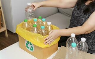 Accueil recycler éco vert zéro concept femme lancement vide Plastique bouteille dans recyclage poubelle avec Jaune des ordures Sacs à maison. photo