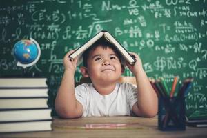 petit garçon réfléchi avec un livre dans la salle de classe