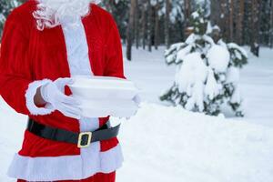 conteneurs de service de livraison de nourriture dans les mains du père noël en plein air dans la neige. promotion de la veille de noël. commande chaude prête à l'emploi, boîte en plastique jetable. restauration des vacances du nouvel an. espace de copie, maquette photo