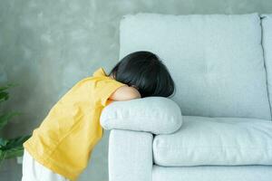 peu asiatique les enfants enfant en jouant cacher et chercher permanent derrière le canapé, adorable enfant ayant amusement dans le maison. content famille avoir amusement avec enfants, activité, apprentissage, activité, jeu, méditation photo