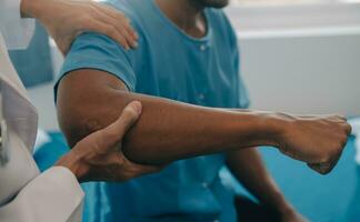 médecin ou physiothérapeute travail examiner traiter blessé bras de athlète Masculin patient, élongation et exercer, Faire le réhabilitation thérapie douleur dans clinique. photo