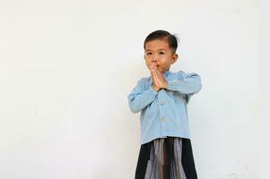 une mignonne timide peu garçon avec bleu chemise et sarong salutation quelqu'un, il se sent embarrassé photo