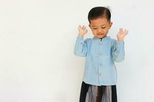 une mignonne Beau peu garçon avec bleu chemise et sarong prier à Allah photo