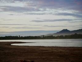 des nuages plus de lac, une vibrant le coucher du soleil plus de une serein lac, avec coloré reflets chatoyant sur le eau, Naturel paysage plus de une courant fonctionnement à rivière avec forêt et montagne, mekong rivière photo