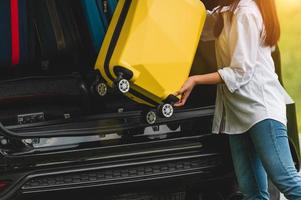 femme asiatique soulevant une valise jaune dans une voiture suv pendant le voyage