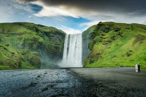 puissant Skogafoss cascade écoulement avec couple touristique profiter dans été à Islande photo