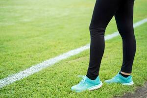 fermer et surgir jambes de Jeune femelle permanent se détendre après faire des exercices et le jogging à le Football stade. photo