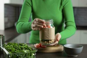 femme fabrication végétalien salade dans pot avec pois chiche. cuisine en bonne santé aliments. photo