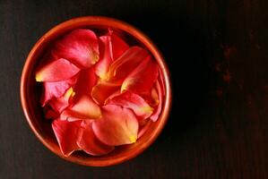 Rose pétales dans une bol sur une foncé en bois Contexte. photo