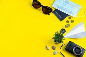 passeport, masque médical et lunettes de soleil sur fond jaune.