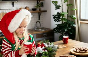 enfant séance sur Noël décoré comptoir. enfant sérieux et à la recherche à rouge agresser avec boisson et bonbons cannes dans photo
