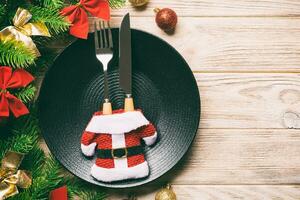 vue de dessus de la fourchette, du couteau et de l'assiette entourés de sapins et de décorations de noël sur fond en bois. concept de réveillon du nouvel an et de dîner de vacances photo