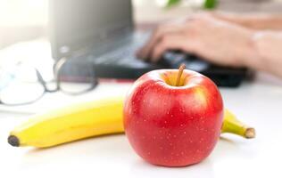 une rouge Pomme et banane sur le bureau. le concept de une en bonne santé nourriture à travail. fermer. sélectif se concentrer. photo