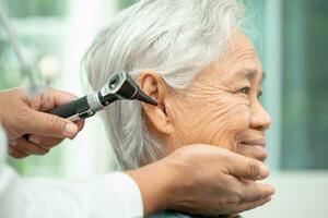 audiologiste ou ent médecin utilisation otoscope vérification oreille de asiatique Sénior femme patient traiter audition perte problème. photo