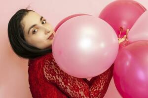 Jeune jolie femme dans rouge soir robe en portant de fête air des ballons. portrait de content Années 20 moyen-orient femelle célébrer valentines jour, anniversaire, fête photo