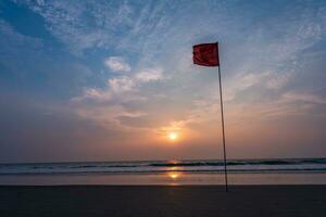 rouge drapeau sur plage sur mer ou océan à le coucher du soleil comme symbole de danger. le mer Etat est pris en considération dangereux et nager est interdit. photo