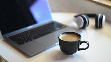 tasse à café avec ordinateur portable flou et casque placé sur une table.