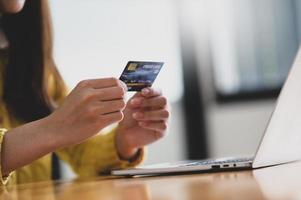 jeune femme tenant une carte de crédit à la main et un ordinateur portable sur la table.