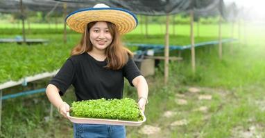 une agricultrice montre un plateau de plants de légumes dans une serre.