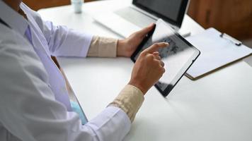 un médecin portant une blouse de laboratoire utilise une tablette.