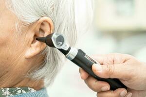 audiologiste ou ent médecin utilisation otoscope vérification oreille de asiatique Sénior femme patient traiter audition perte problème. photo