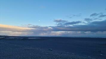 islandais noir le sable plage à le coucher du soleil avec d'or rose ciel et glacial des champs offre magique paysage. nord Région avec énorme océan de face littoral dans fantastique environnement. photo