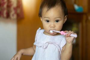 11 mois fille pratiquant une brosse à dents par se de sa de la mère enseignement. photo