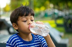 enfant en buvant l'eau de une transparent Plastique bouteille. photo