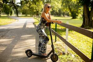 Jeune femme avec un électrique scooter dans le parc sur une ensoleillé été journée photo