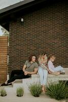 famille avec une mère, père et fille séance à l'extérieur sur le pas de une de face porche de une brique maison photo