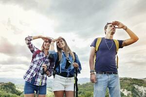 groupe de Jeune adultes regards à le horizon pendant randonnée photo