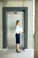 Jeune affaires femme avec portable attendre pour ascenseur dans le Bureau couloir photo