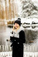 Jeune femme dans chaud vêtements profiter dans neige avec à emporter café tasse photo