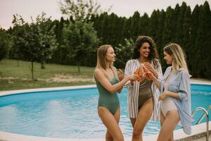 Trois femmes prendre plaisir une relaxant journée par le nager piscine, sirotant sur rafraîchissant Cidre photo