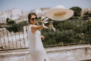 une Jeune femme dans une blanc robe jeter chapeau pendant touristique visite dans alborebello, Italie photo