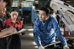 asiatique Masculin professionnel automobile ingénieur superviseur décrit voiture moteur entretien et réparation travail avec mécanicien ouvrier états-majors équipe dans réparer un service garage, spécialiste métiers dans auto industrie. photo