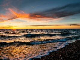 le coucher du soleil plus de le mer avec vagues dans le premier plan photo