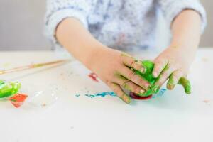 une enfant met une vert Pâques Oeuf sur une supporter avec le sien mains coloré avec peindre sur une blanc tableau. photo