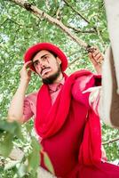 une triste mime est séance sur une arbre dans rouge vêtements. pitre dans pensée sur une bouleau. photo