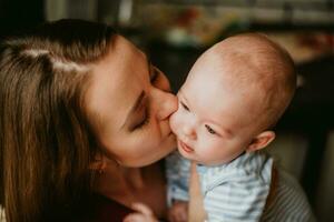 une mère détient une bébé dans sa bras. une maman baisers une nourrisson. une femmes câlins sa tout-petit. une fille a amusement et se réjouit avec le enfant. photo